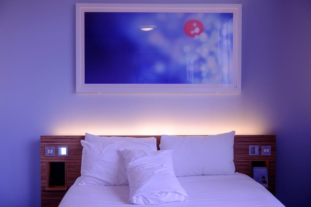 A close up of a hotel bed. Framed art and a white wall in the background. 