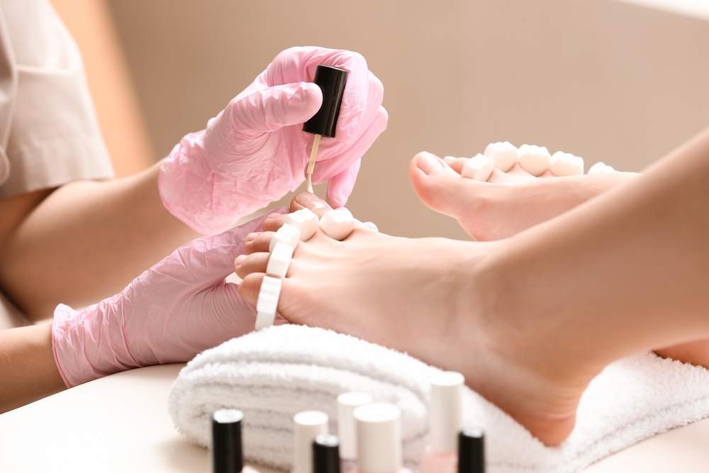 Young woman getting pedicure with nail polish in beauty salon, closeup