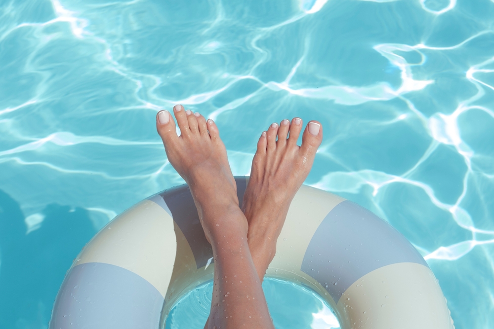 Slim woman legs on the hotel swimming pool.