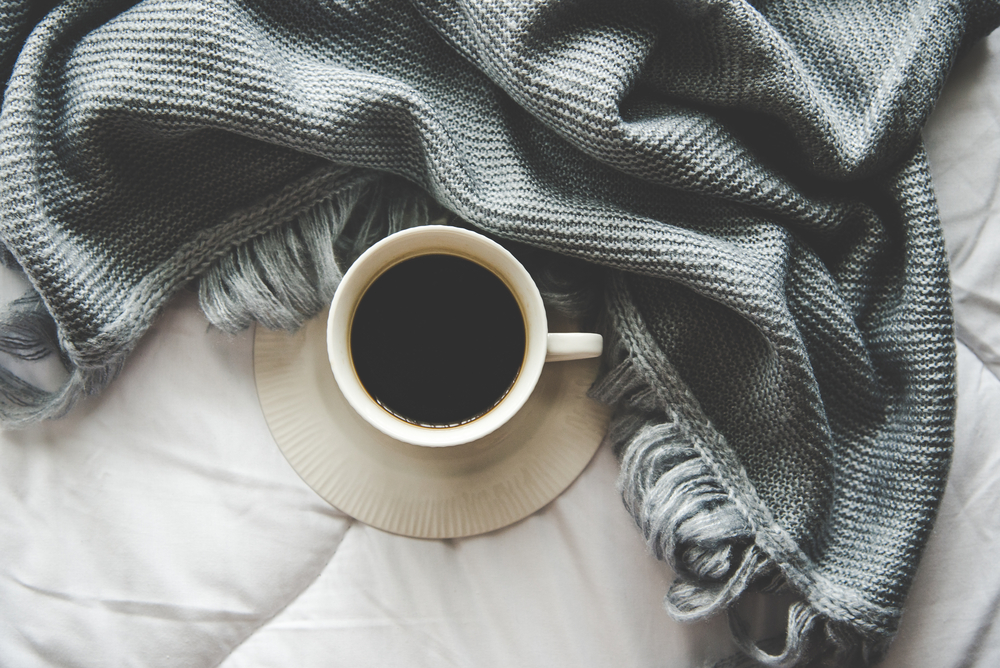 Coffee with Cozy winter interior home background, cup of hot tea marshmallow, warm knitted sweater on white bed background, vintage tone. Lifestyle concept.
